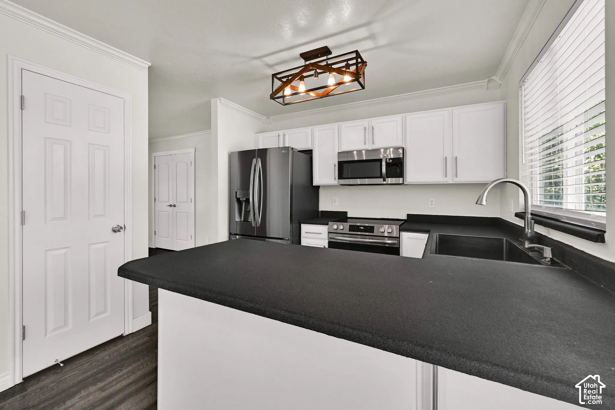 Kitchen featuring white shaker-style cabinetry, dark stone-finish countertops, stainless steel appliances, dark wood-finish flooring, and a rectangular metal-frame light fixture