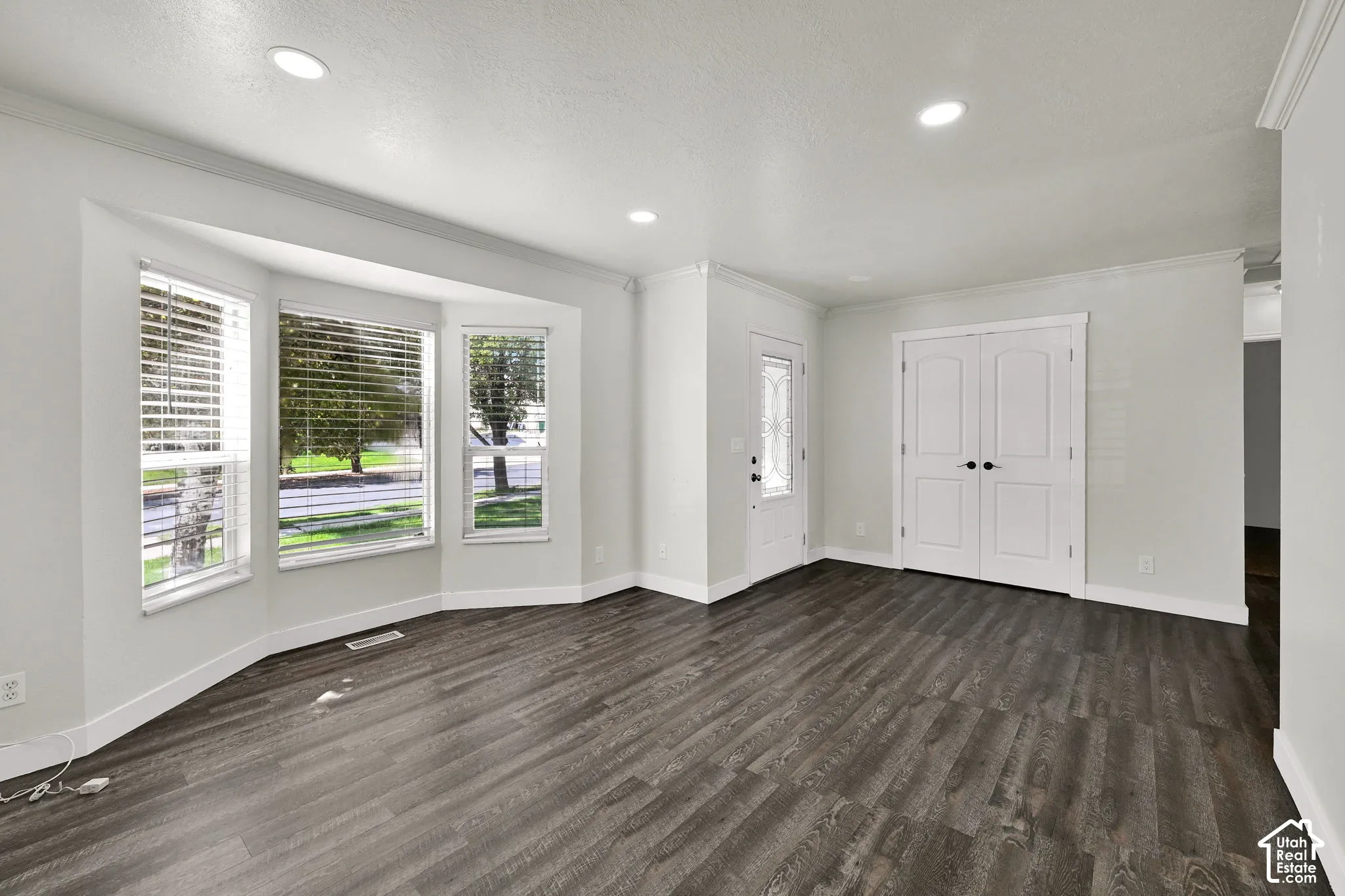 Open-concept living space featuring wood-finish flooring, a bay window, recessed ceiling lighting, crown molding, and double doors