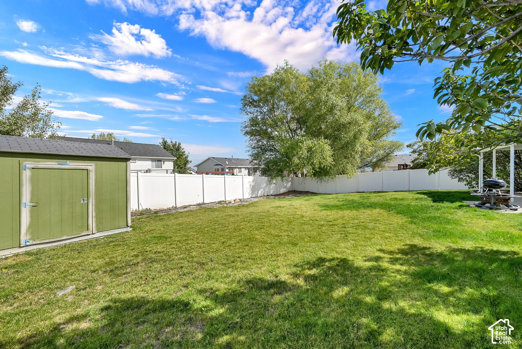 Fenced backyard featuring a manicured lawn, mature trees, and a detached storage shed