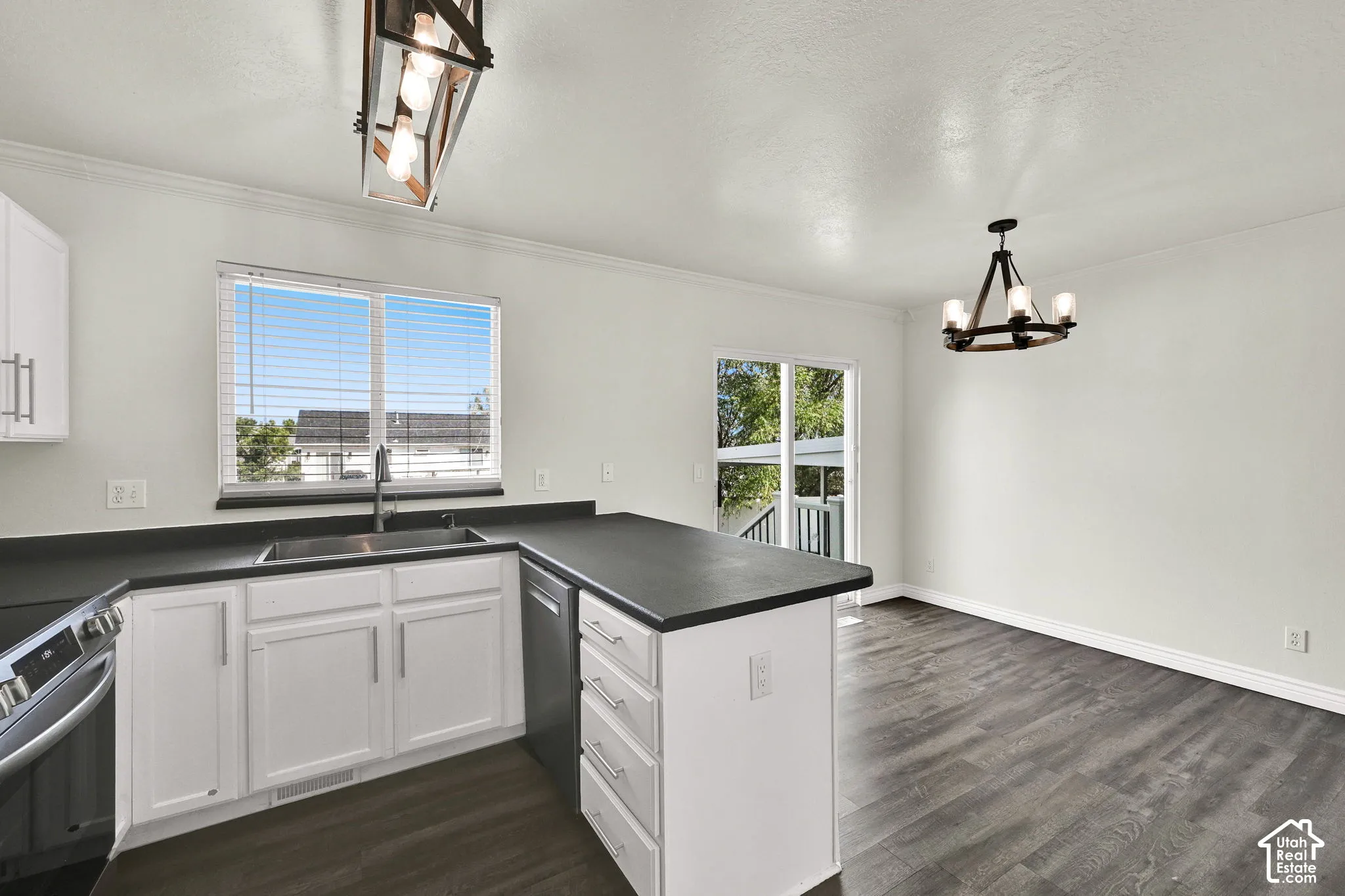 Kitchen featuring white shaker-style cabinetry, matte black countertops, wood-finish flooring, and dual hanging light fixtures