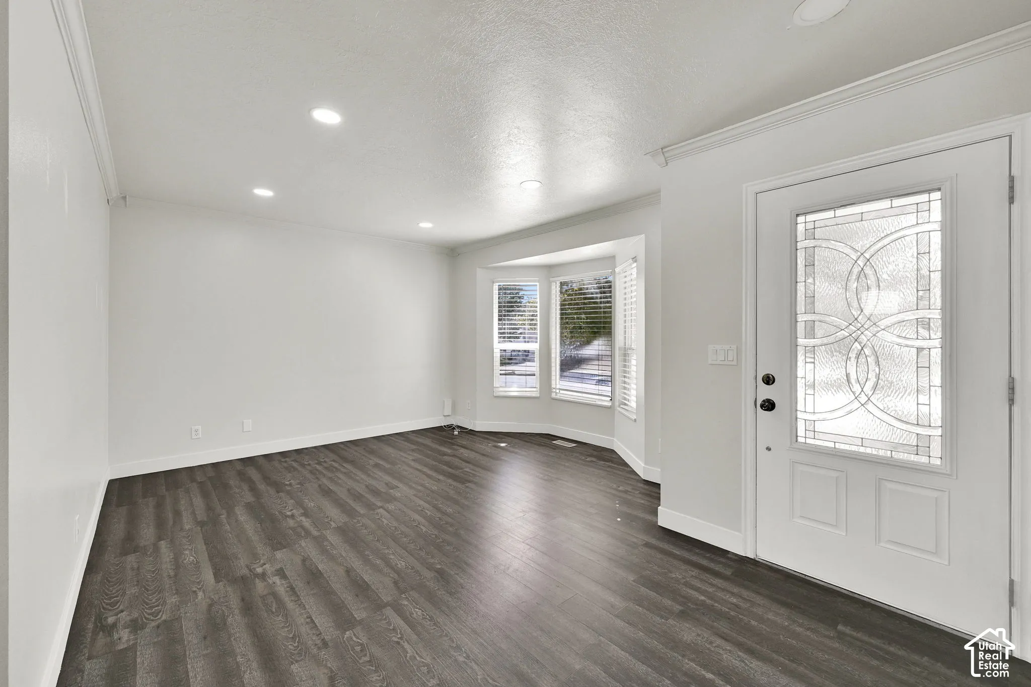 Wood-finish flooring, bay window, recessed ceiling lighting, crown molding, and front entry door with decorative glass inlay