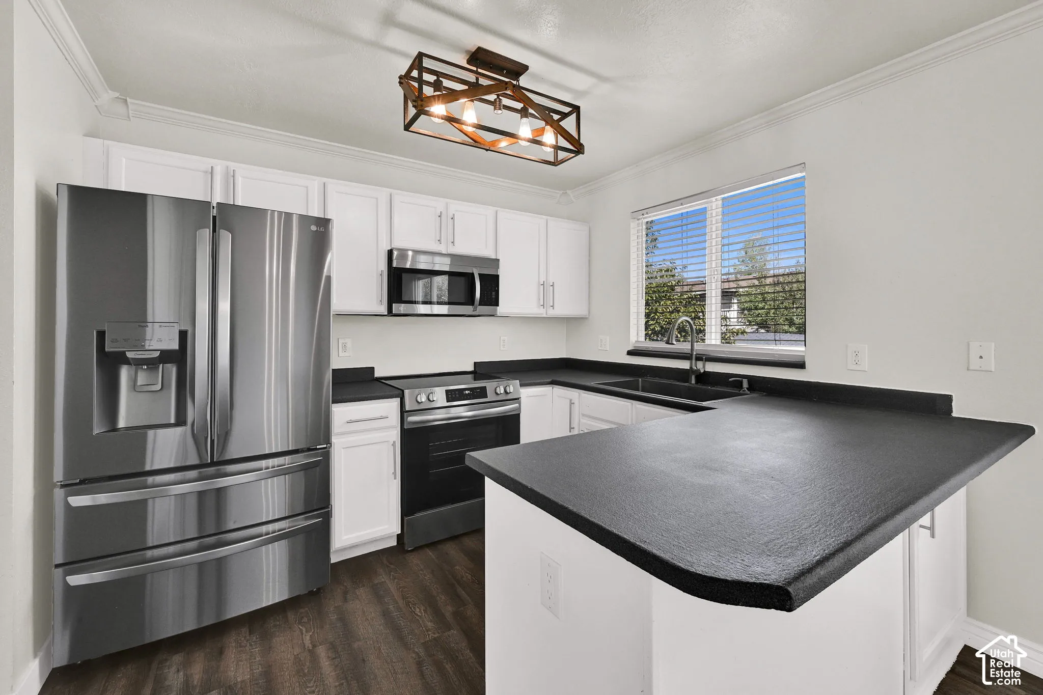 Kitchen featuring white cabinetry, dark solid-surface countertops, wood-finish flooring, stainless steel appliances, and a geometric-frame pendant light
