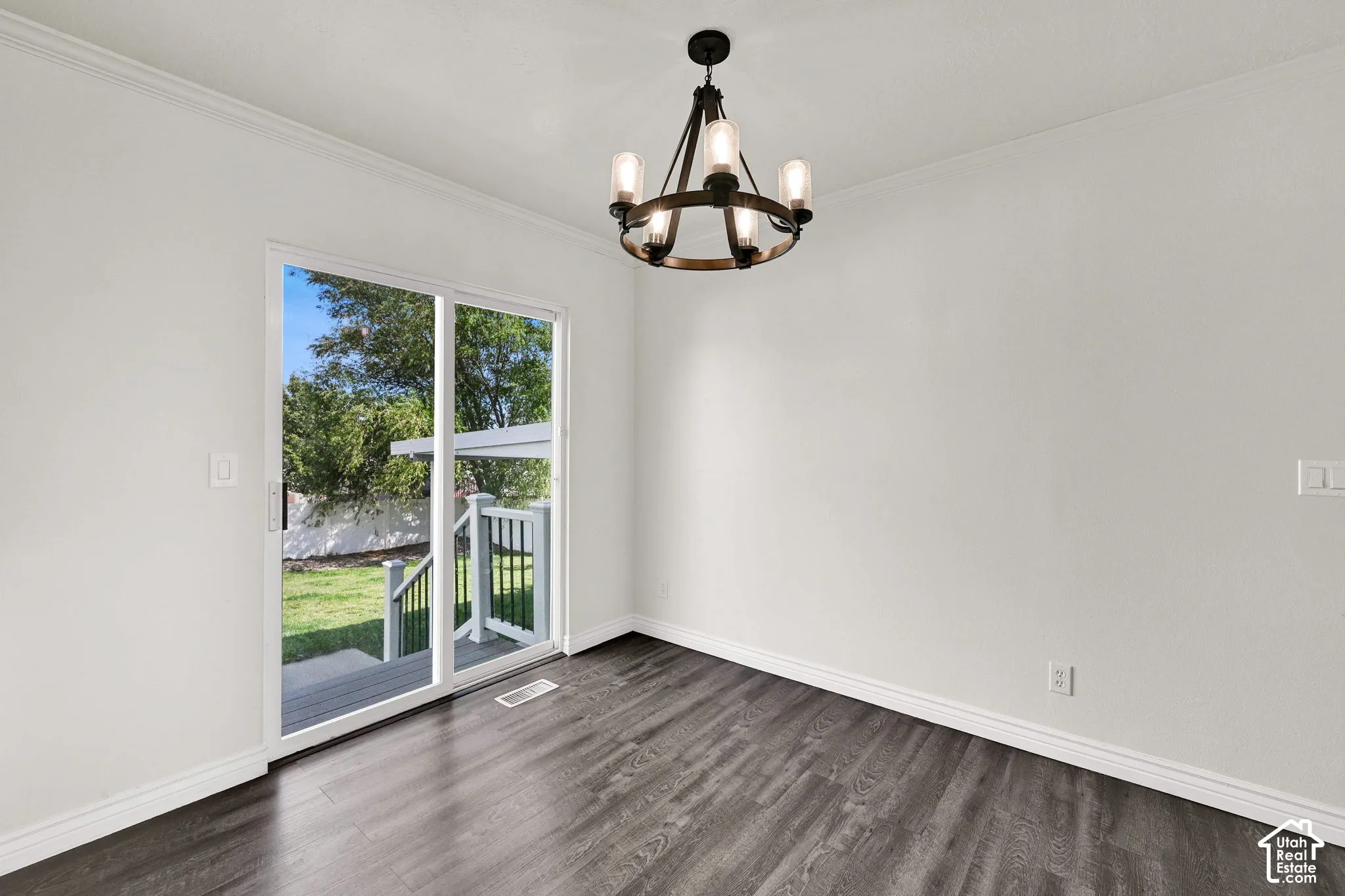 Wood-finish flooring, metal-frame five-light chandelier, and glass sliding door providing access to an exterior deck