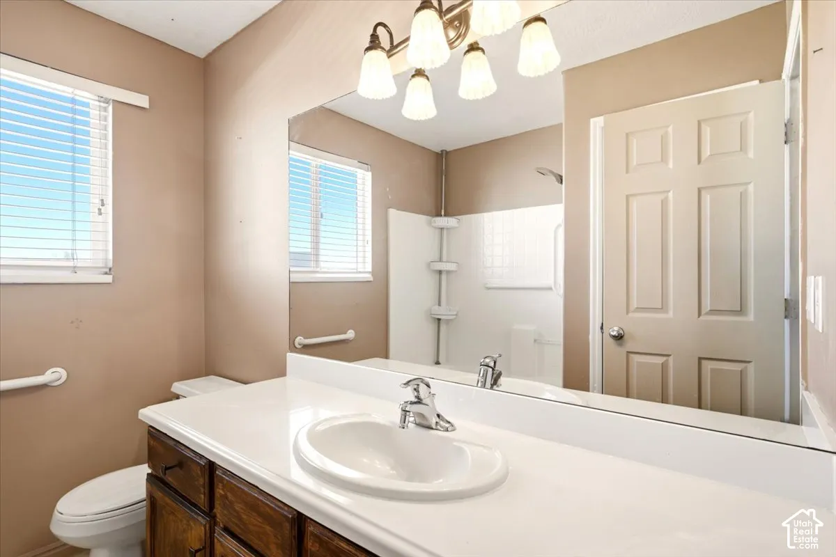 Bathroom featuring a white integrated countertop and sink, wood-finish cabinetry, a large wall-mounted vanity mirror, a multi-bulb light fixture, and a white tub-and-shower surround