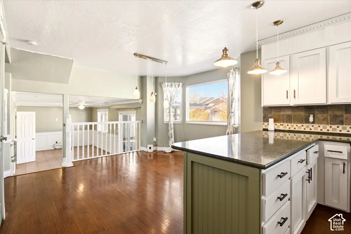 Kitchen featuring a stone-surface island, beadboard cabinetry, stone tile backsplash, wood-finish flooring, and pendant lighting