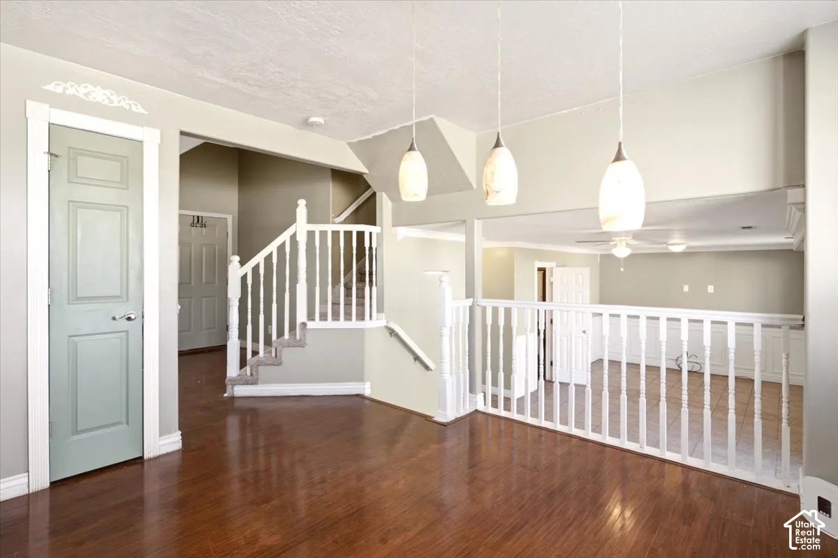 Dark wood-finish flooring, white staircase with baluster railing, tiered floor plan with neutral wall tones, and three decorative pendant light fixtures