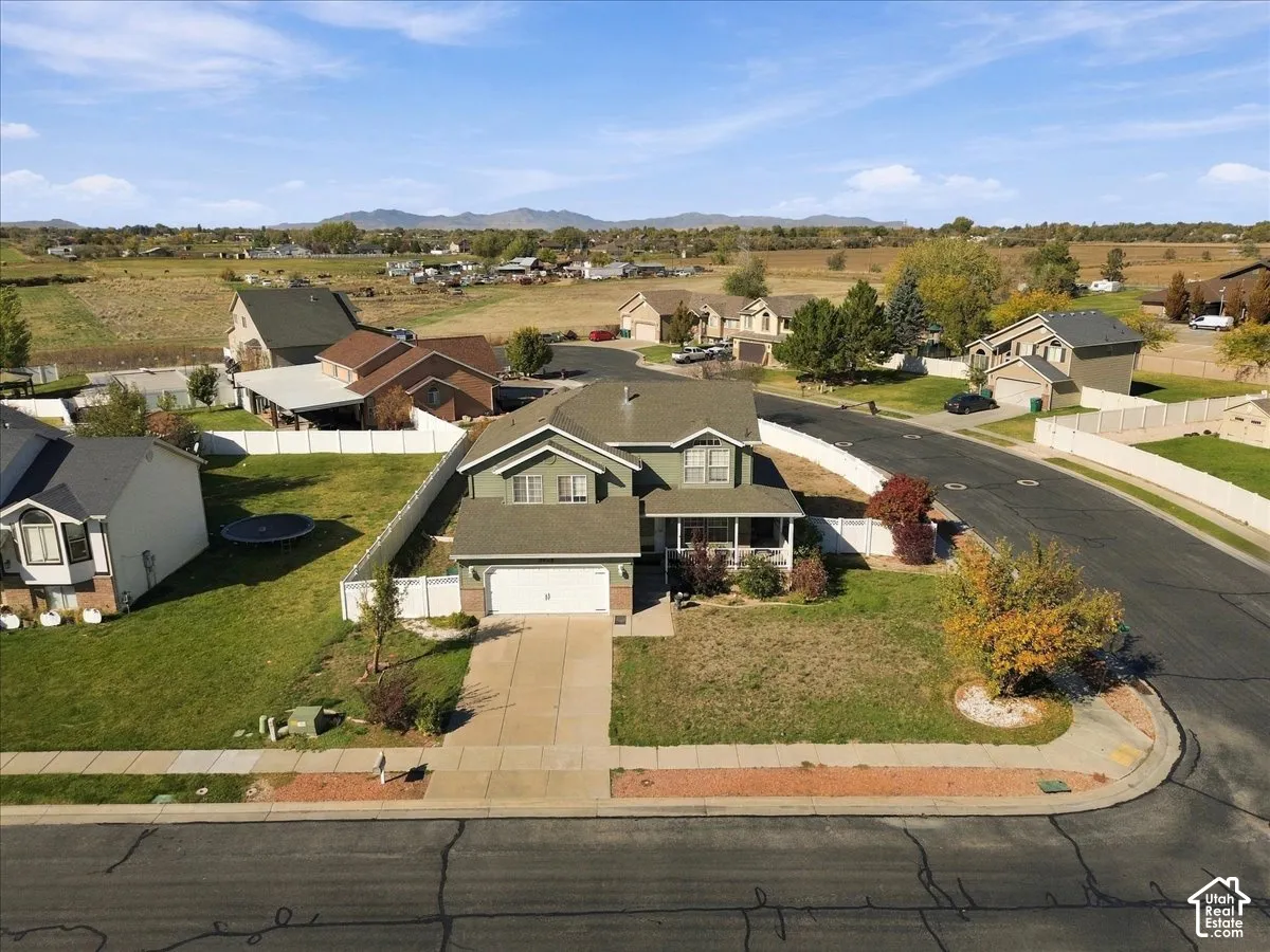 Two-story residence featuring a multi-gabled roofline, front-facing two-car garage, concrete driveway, white vinyl perimeter fencing, and expansive mountain terrain backdrop