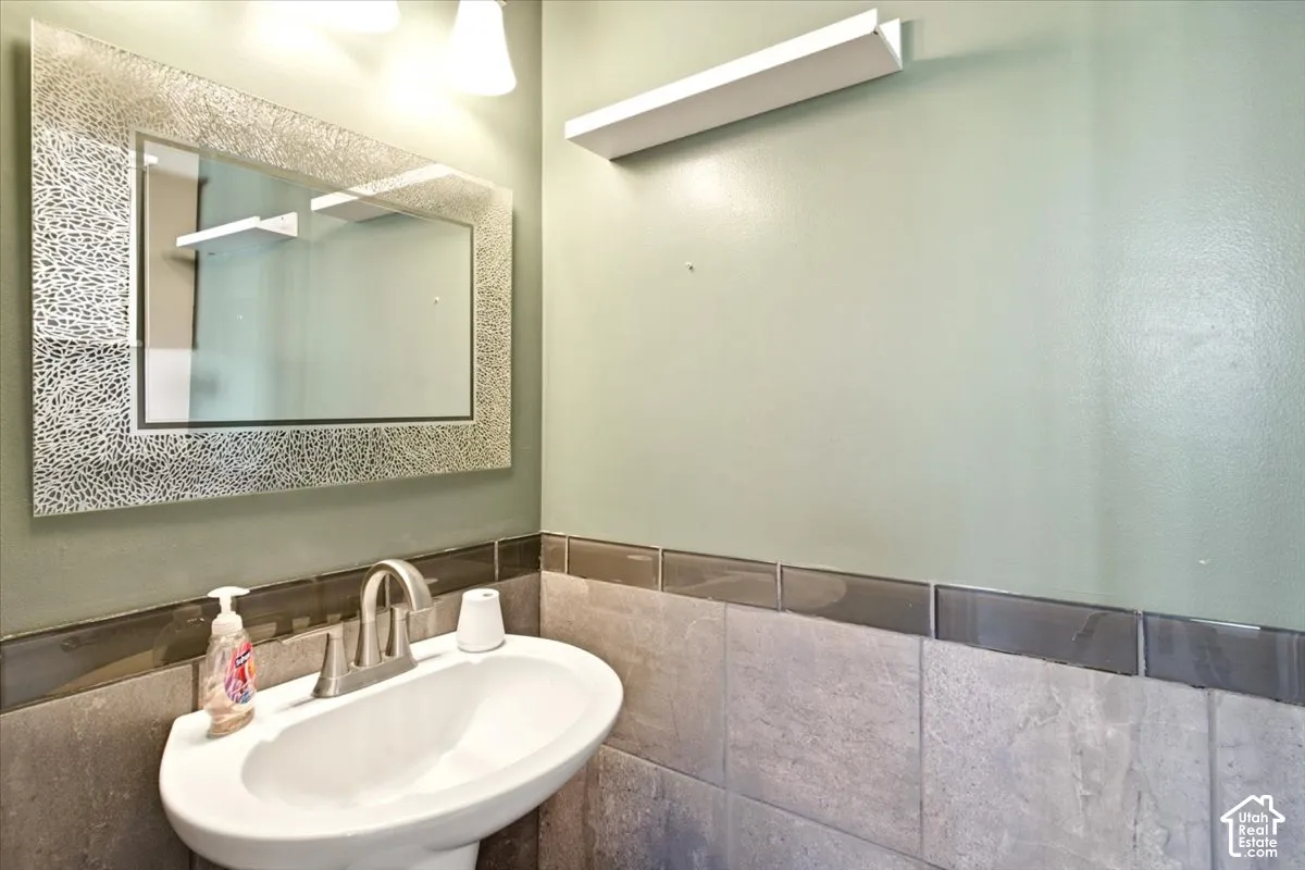 Wall-mounted vanity sink with a metallic-finish faucet, framed decorative mirror, and neutral stone-tiled wainscoting with a dark glass accent border