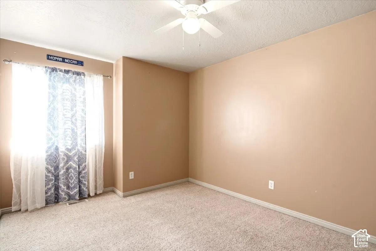 Interior room featuring neutral-toned walls, wall-to-wall carpeting, and a ceiling-mounted fan with integrated lighting fixture