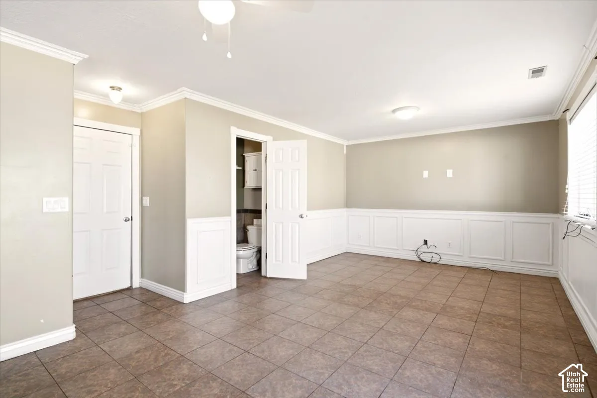 Interior space featuring ceramic tile flooring, white wainscoting, crown molding, and two interior doors with overhead lighting fixtures