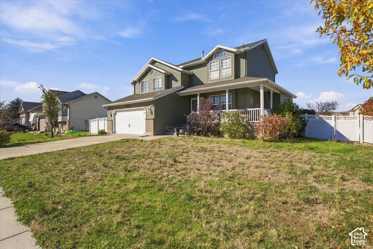 Two-story exterior featuring vinyl siding, a covered front porch with white railing, a two-car garage, and a white privacy fence