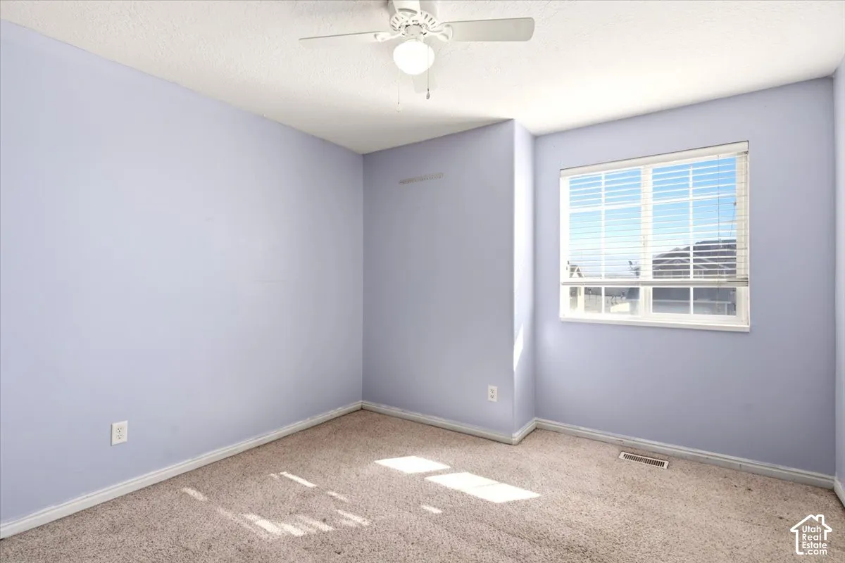 Room featuring light-toned carpeting, neutral wall color, and a ceiling-mounted light fixture with an integrated fan