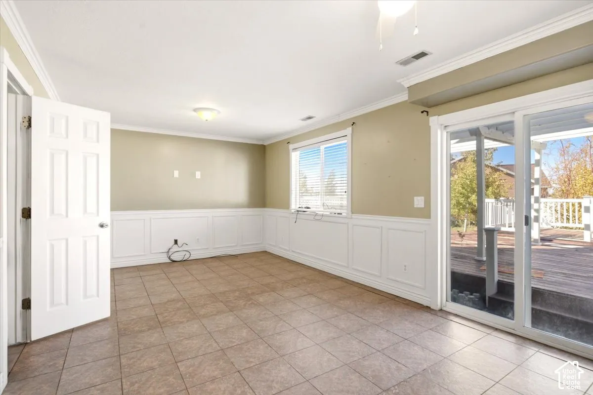 Interior space featuring tile flooring, white wainscoting, crown molding, and sliding glass doors with access to an exterior wood deck