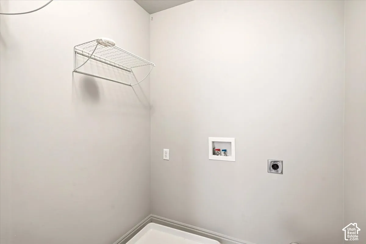 Dedicated utility space featuring a wall-mounted wire storage shelf, recessed water supply box, dedicated electrical outlet, and an exhaust vent