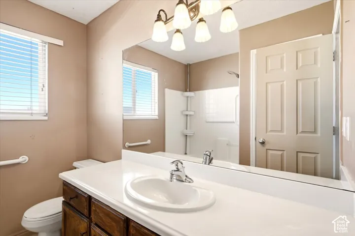 Bathroom featuring a white integrated countertop and sink, wood-finish cabinetry, a large wall-mounted vanity mirror, a multi-bulb light fixture, and a white tub-and-shower surround