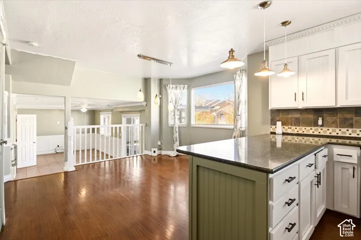 Kitchen featuring a stone-surface island, beadboard cabinetry, stone tile backsplash, wood-finish flooring, and pendant lighting