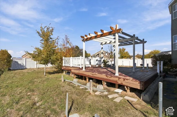 Backyard featuring a wood-deck platform, overhead pergola, white vinyl fencing, and a grassy lawn area