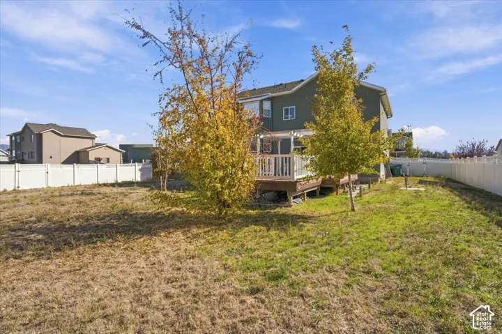 Expansive backyard featuring a raised wooden deck with a pergola, perimeter vinyl fencing, and mature trees