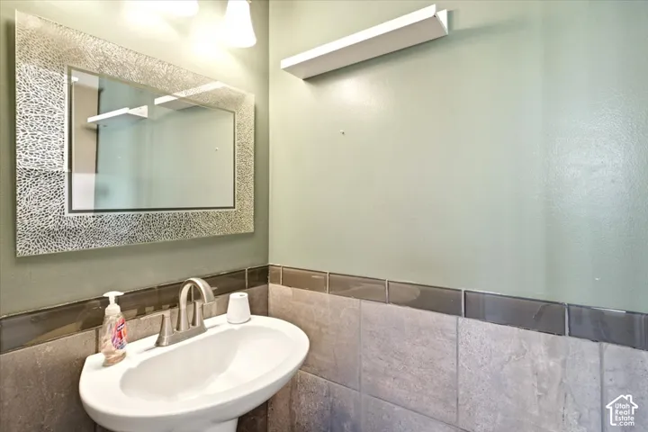 Wall-mounted vanity sink with a metallic-finish faucet, framed decorative mirror, and neutral stone-tiled wainscoting with a dark glass accent border