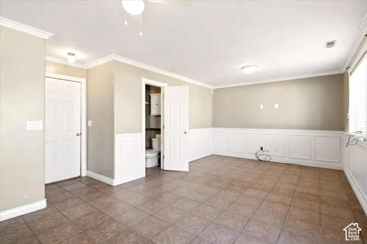 Interior space featuring ceramic tile flooring, white wainscoting, crown molding, and two interior doors with overhead lighting fixtures