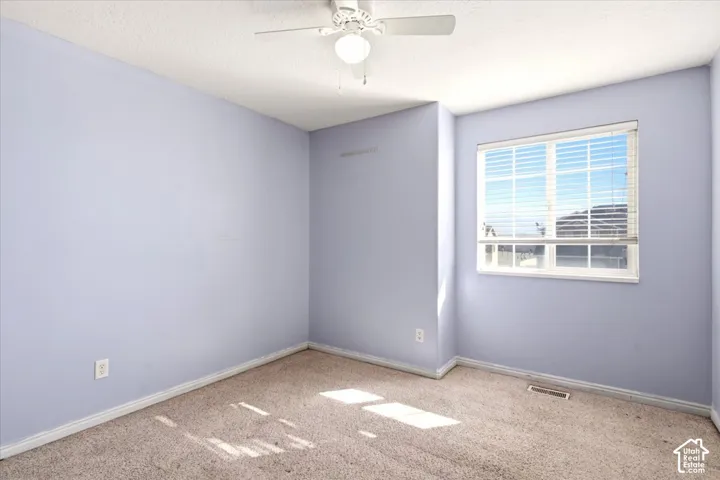 Room featuring light-toned carpeting, neutral wall color, and a ceiling-mounted light fixture with an integrated fan