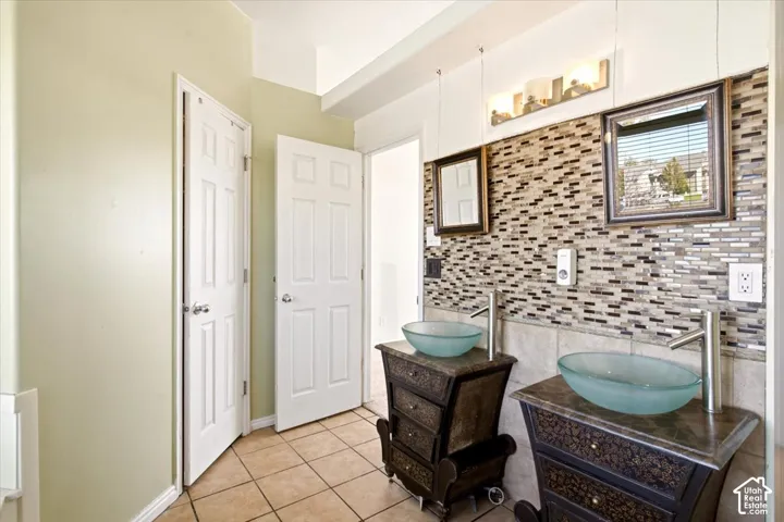 Double vanity featuring ornate cabinetry, glass vessel sinks, stone-finish countertops, and a mosaic tile backsplash