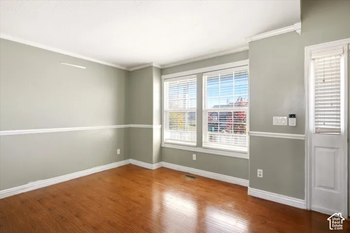 Room featuring wood-finish flooring, white crown molding, chair rail trim, and dual windows with horizontal blinds