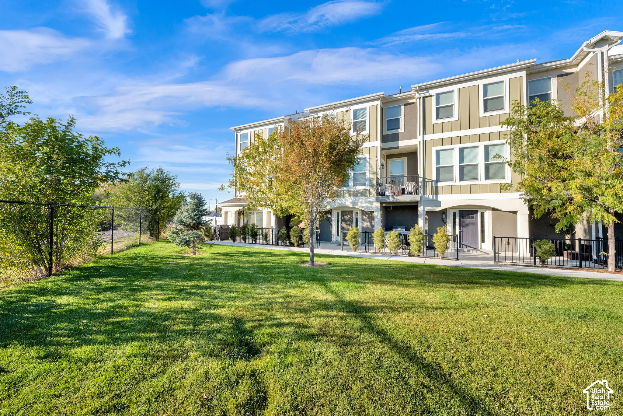 Multi-story exterior featuring vertical board-and-batten siding, private elevated balconies, black metal fencing, and an expansive lawn