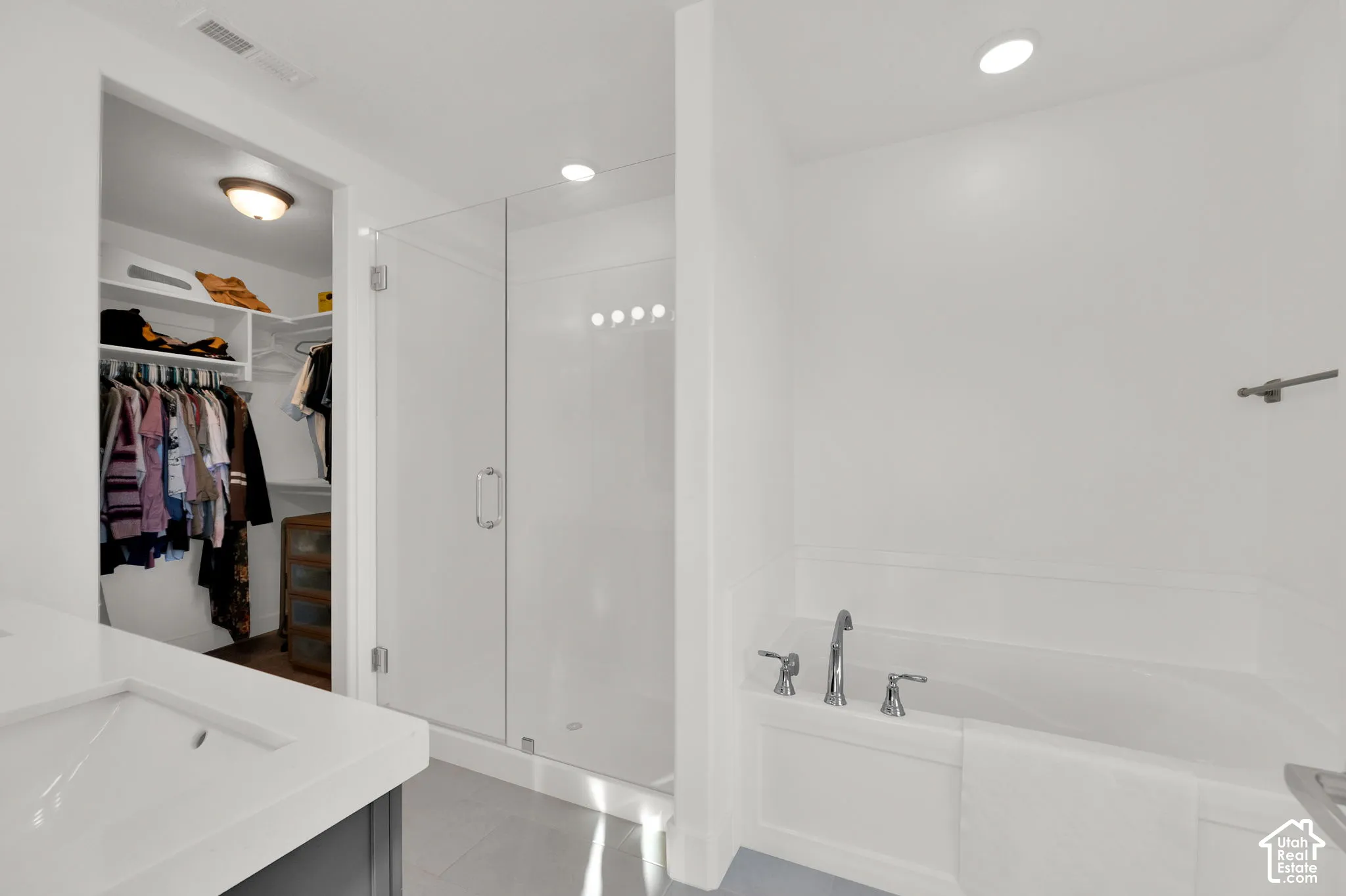 Bathroom featuring a solid-surface vanity, walk-in shower with a glass enclosure, a deep soaking tub with polished chrome fixtures, and a walk-in closet with built-in shelving