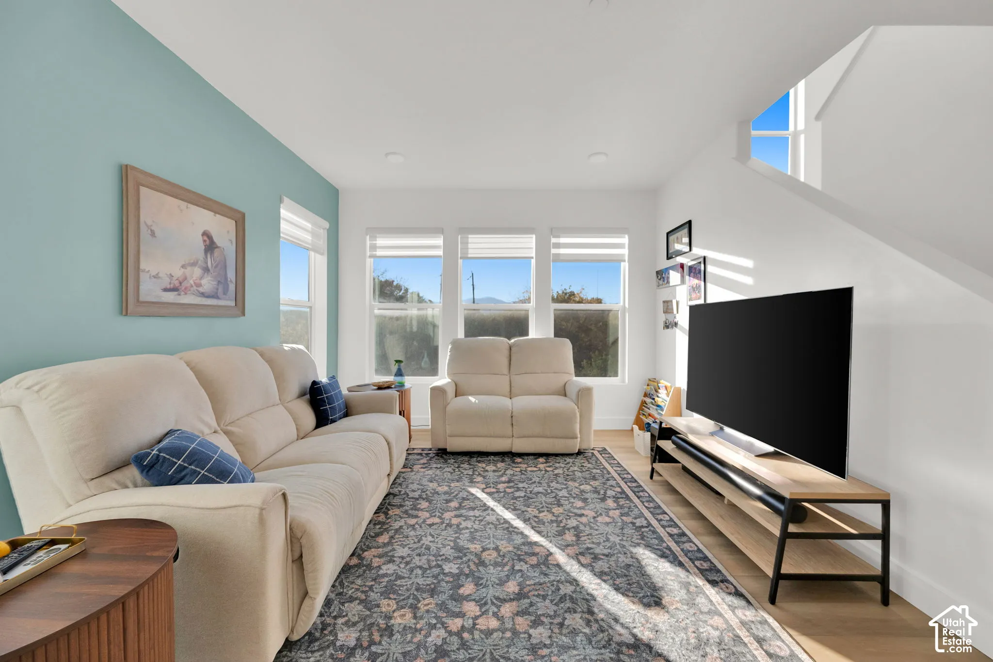 Living area featuring wood-finish flooring, recessed lighting, and a trio of large windows with integrated blinds