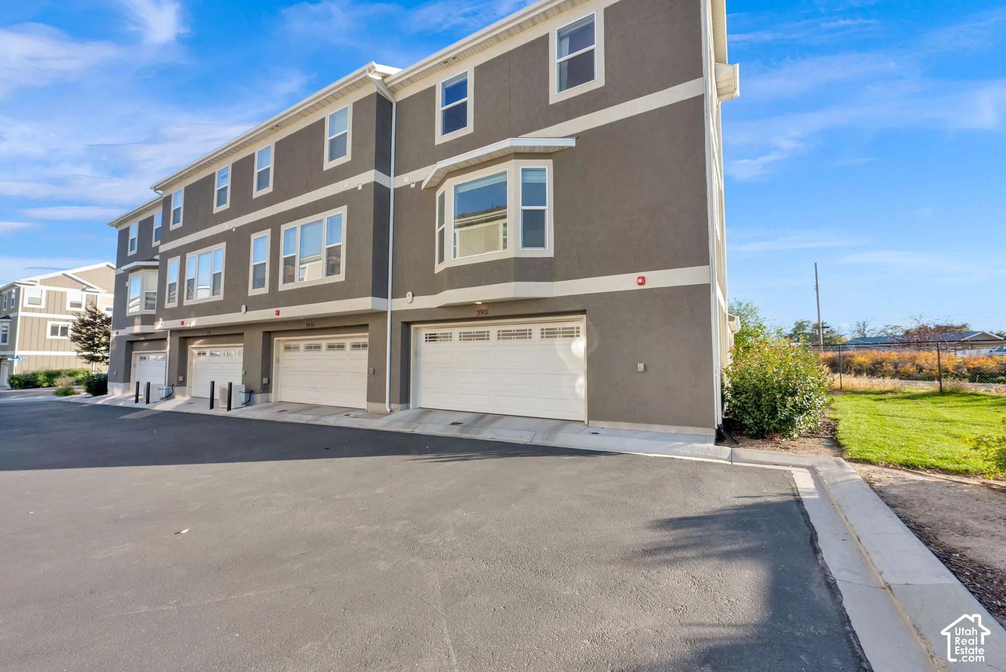 Multi-story townhome exterior featuring stucco siding, white-trimmed paneled garage doors, bay windows, and asphalt driveway