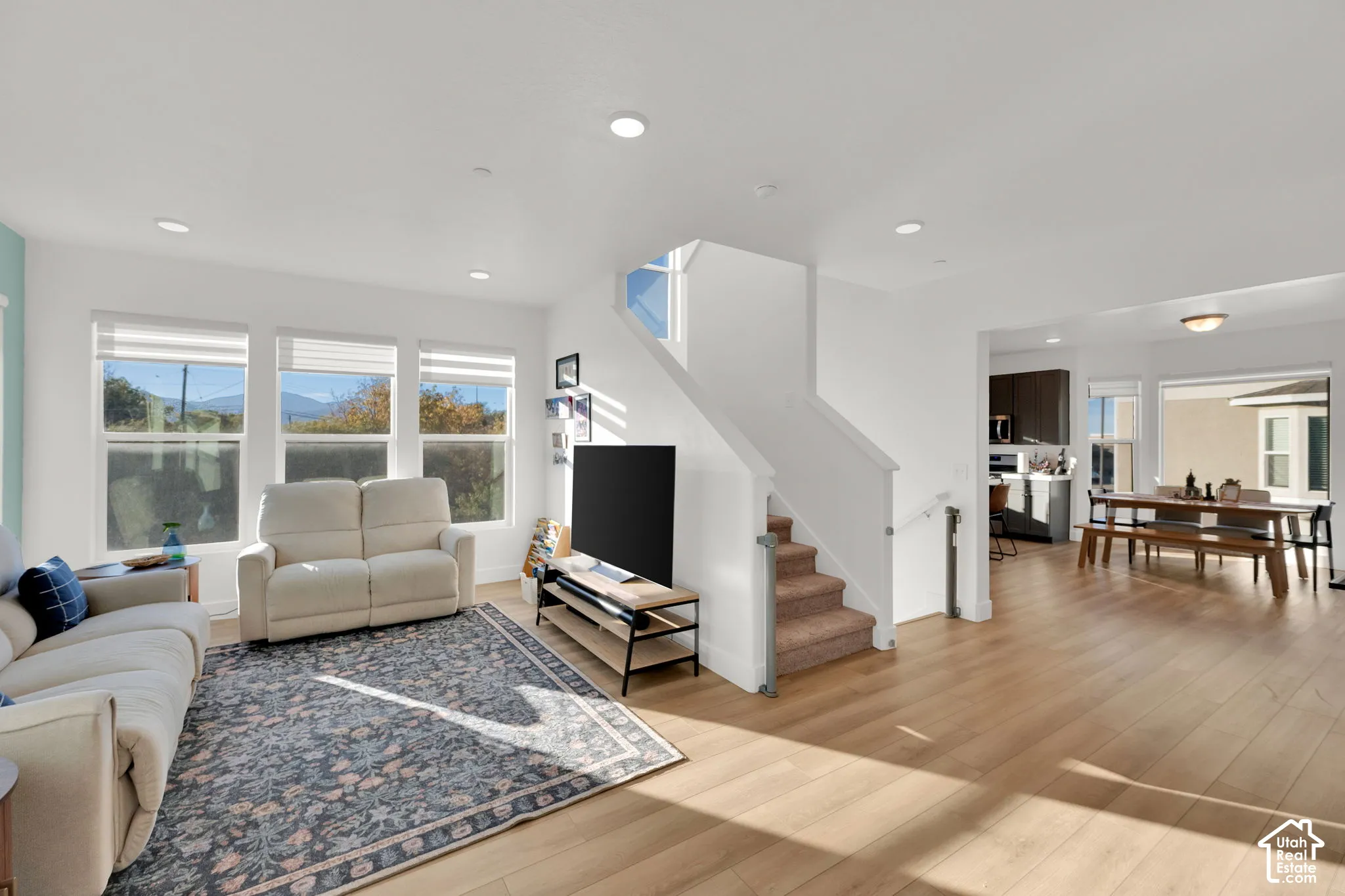 Open-concept interior featuring wood-finish flooring, recessed lighting, and large windows with horizontal blinds
