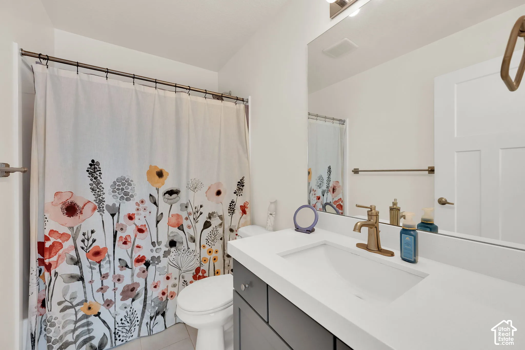 Bathroom featuring a charcoal-toned vanity, white countertop with an integrated basin, brass-finish faucet, and full-width vanity mirror