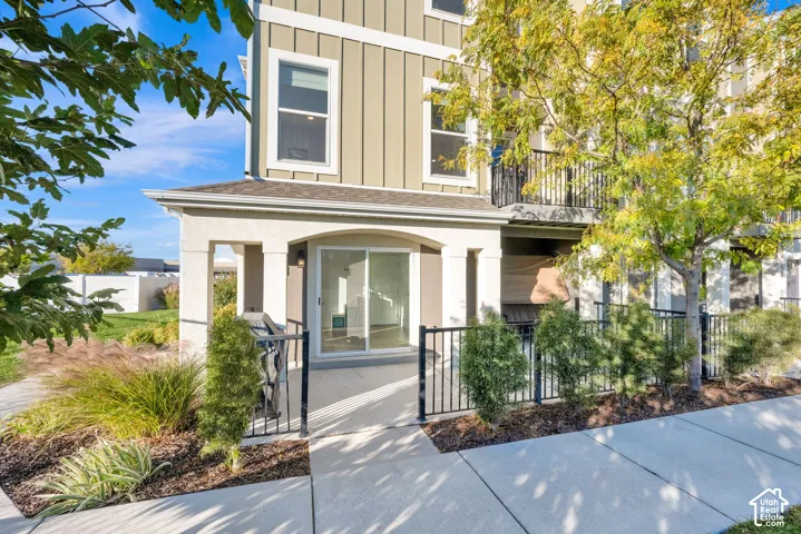 Multi-story exterior featuring board and batten siding, a covered concrete patio, sliding glass door, and a black metal perimeter fence