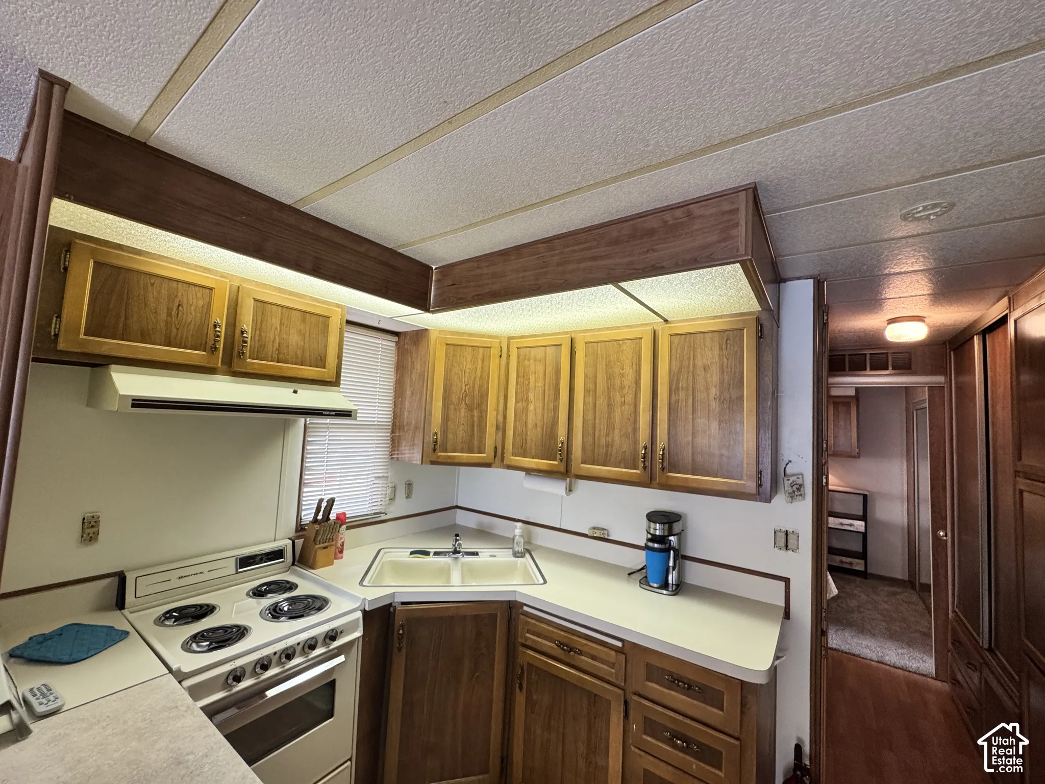 Kitchen featuring wood cabinetry, integrated range hood, white countertop, dual-basin sink, and built-in electric range