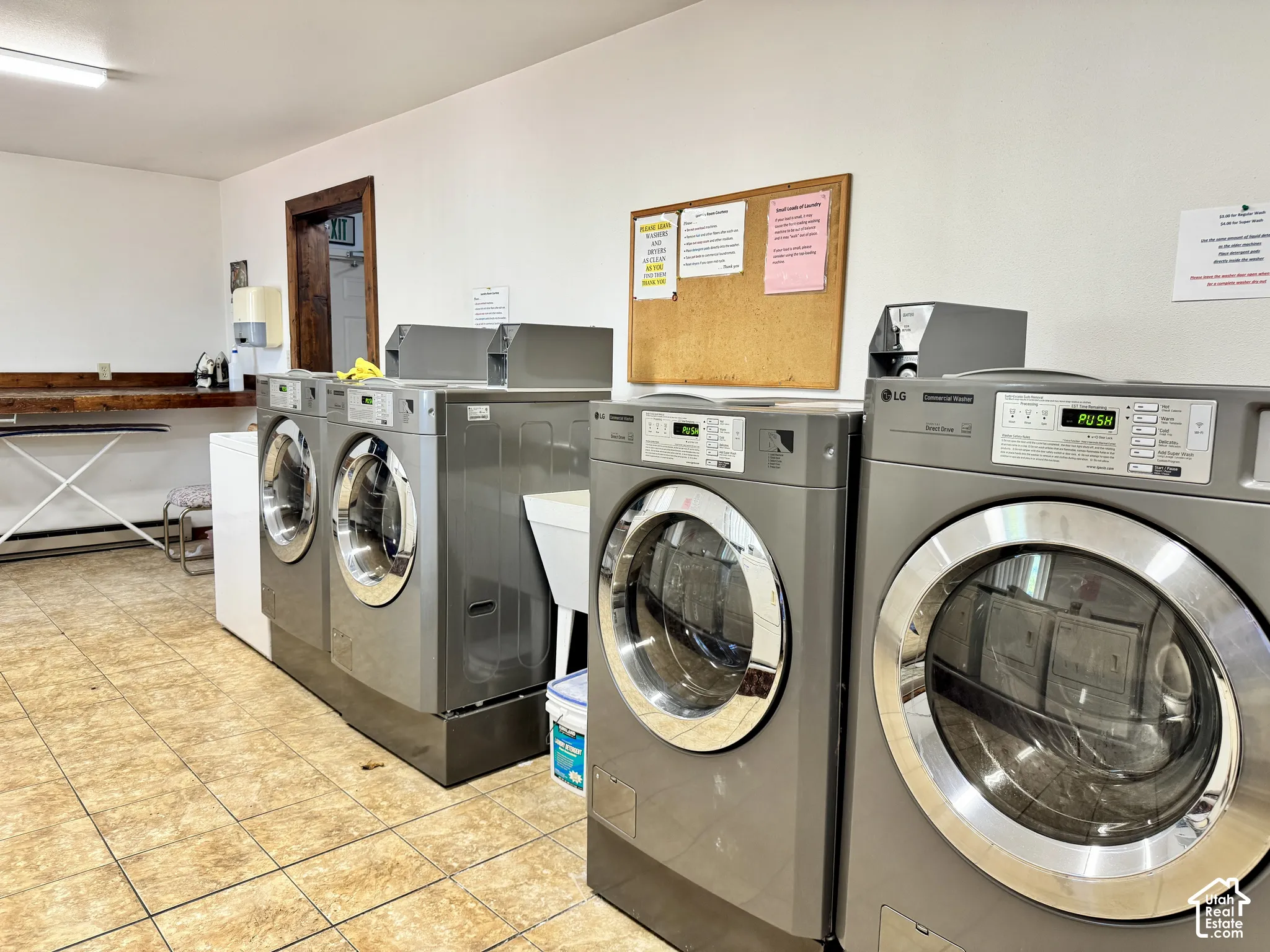 Utility area featuring tile flooring, a white porcelain utility sink, and multiple front-load coin-operated washing machines