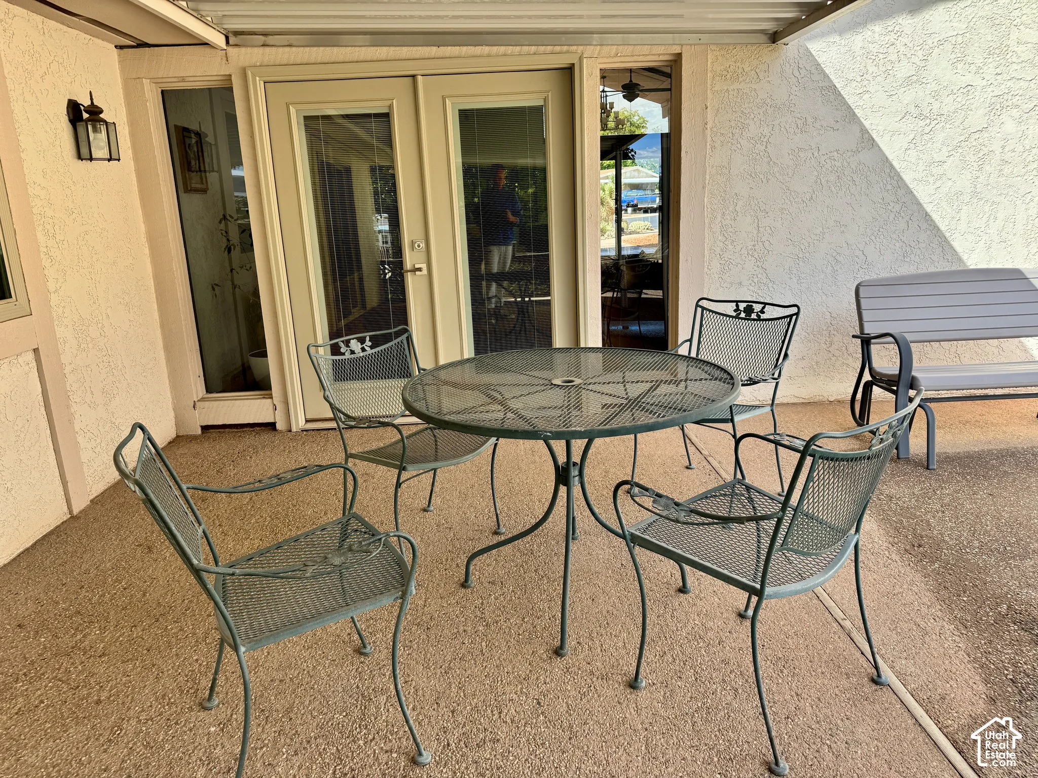 Covered patio featuring concrete flooring, stucco exterior walls, dual-glass panel doors with sidelights, and a wall-mounted light fixture