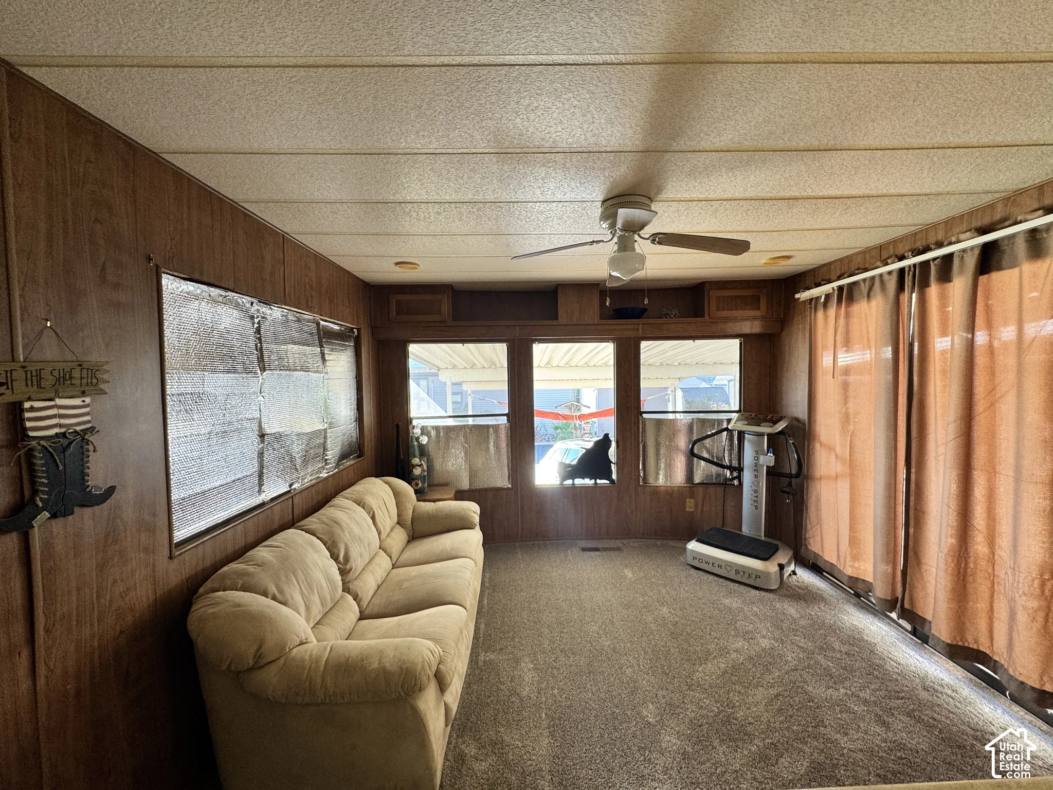 Wood-paneled interior space featuring integrated overhead storage cabinets, a ceiling fan with light fixture, and large multi-pane windows
