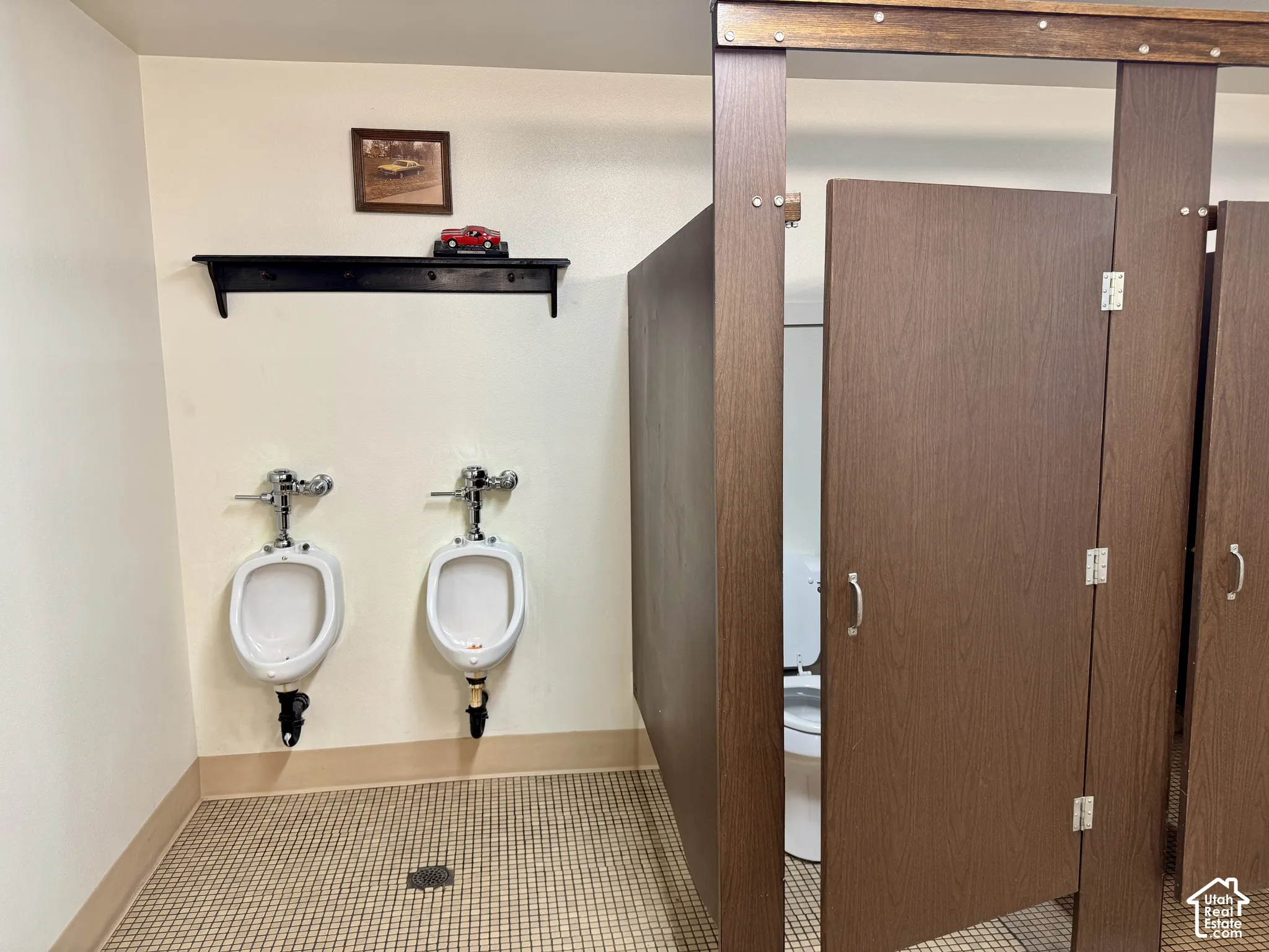 Restroom featuring wall-mounted porcelain urinals, a wood-finish privacy partition, and mosaic tile flooring