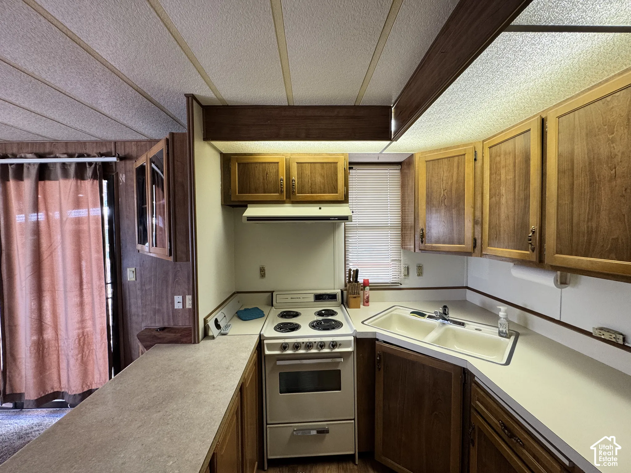 Kitchen featuring wood cabinetry, a four-burner electric range, an integrated range hood, solid-surface countertops, and a double-basin sink