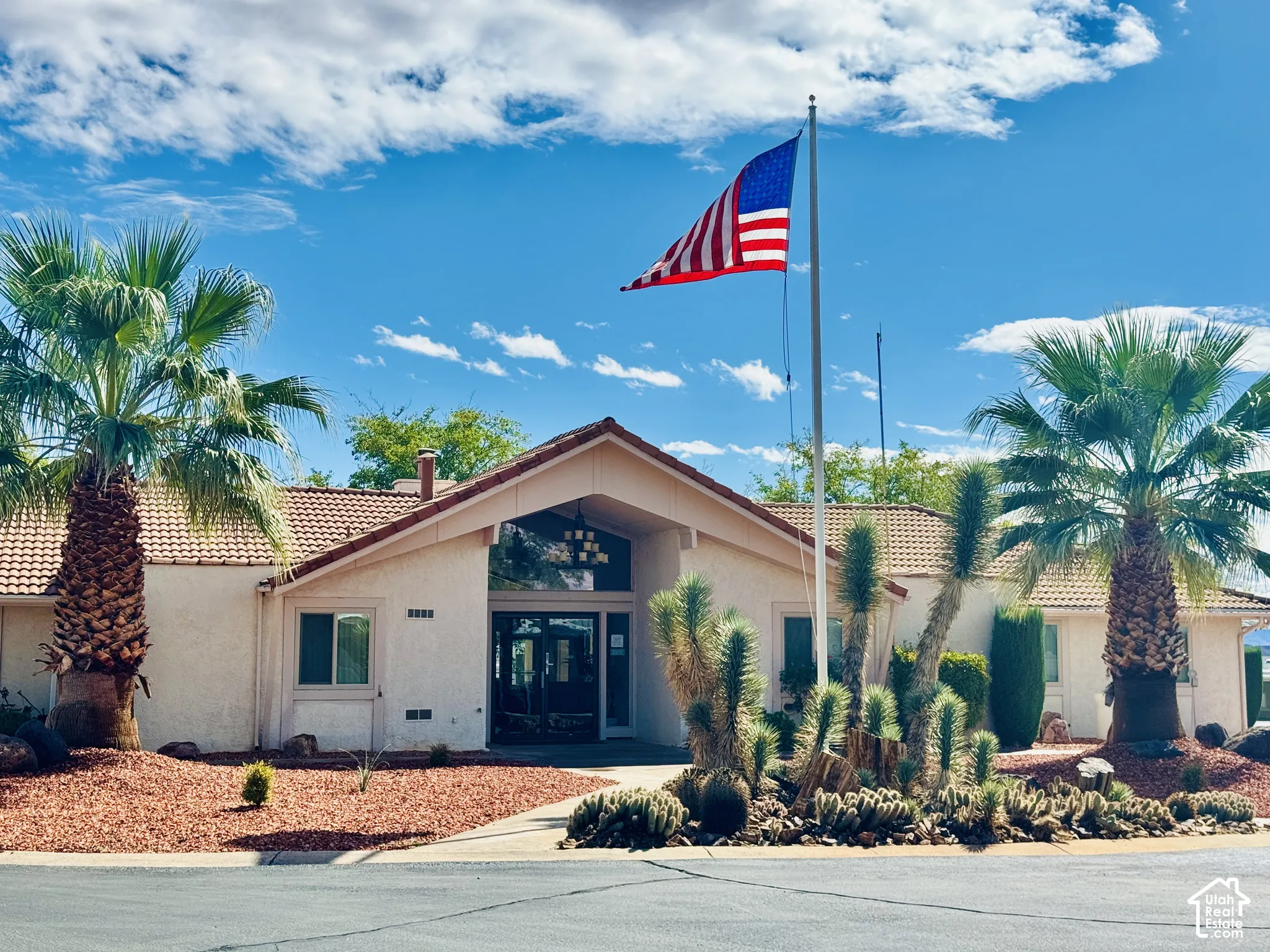 Stucco exterior featuring a tiled roof, recessed entryway, and xeriscaped front yard with mature palm trees and desert vegetation