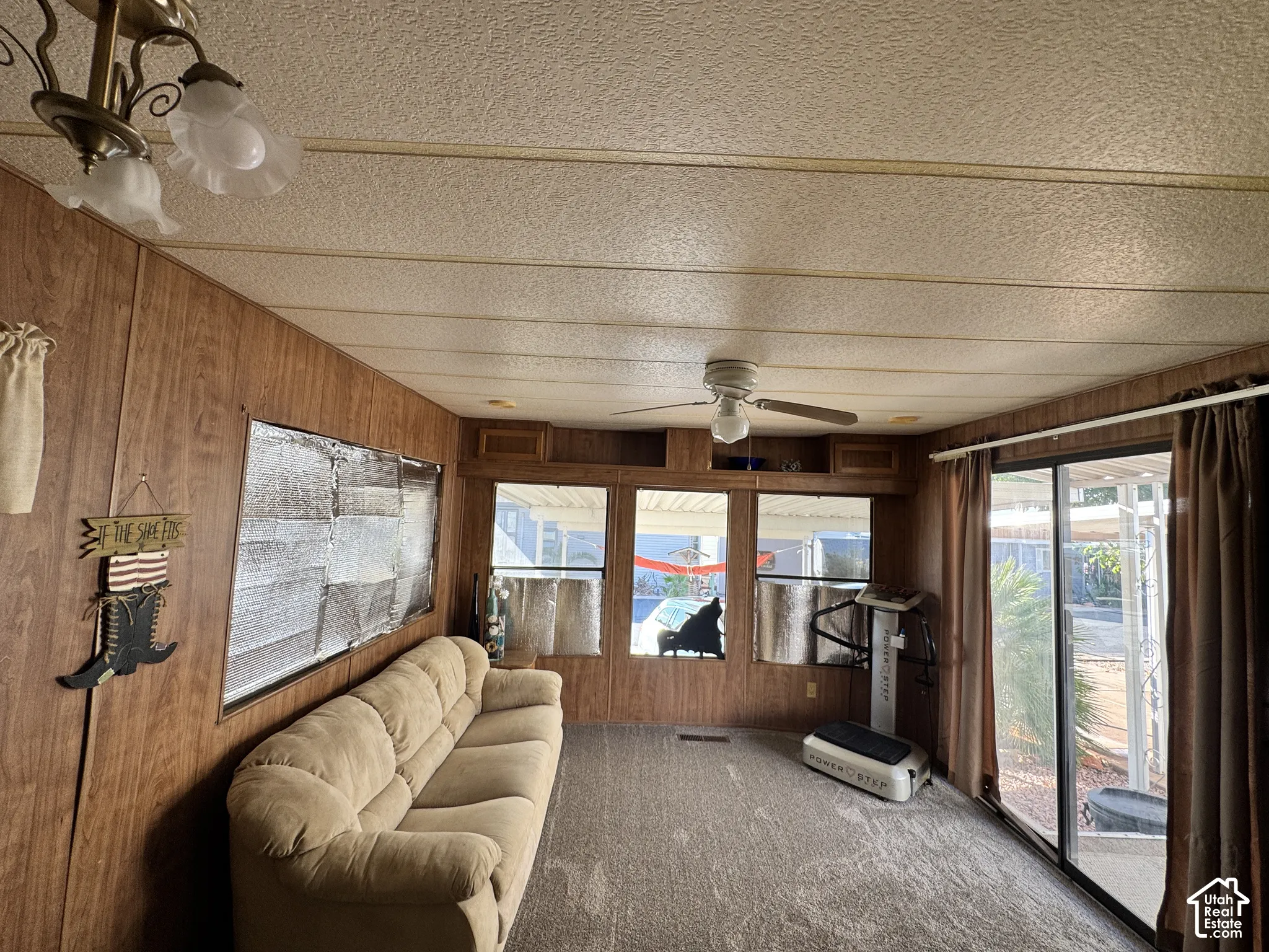 Interior space featuring wood-finish wall paneling, ceiling fan with integrated lighting, oversized windows, and sliding glass door