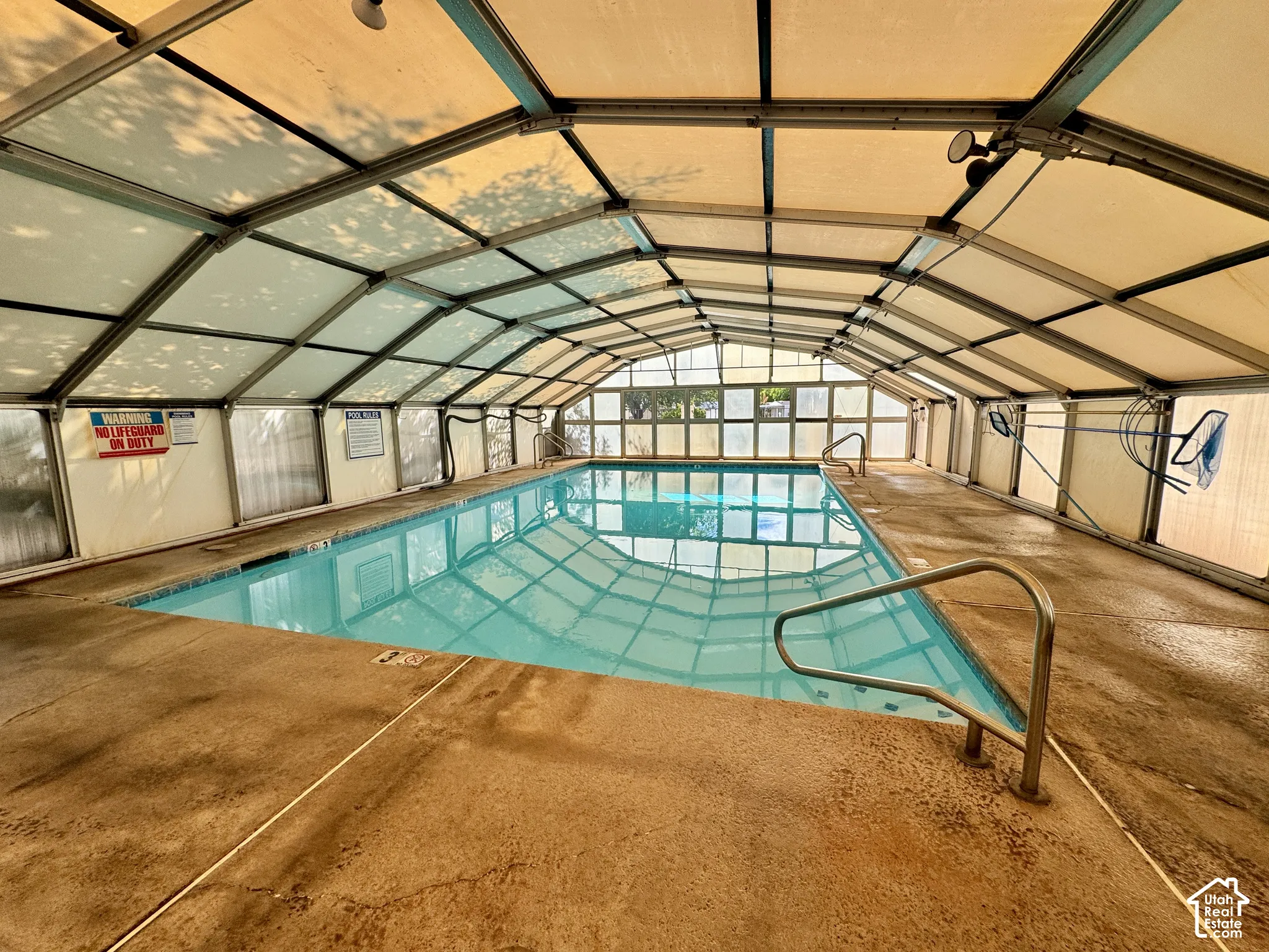 Enclosed indoor swimming pool featuring a retractable arched structure, concrete deck, and metal handrails