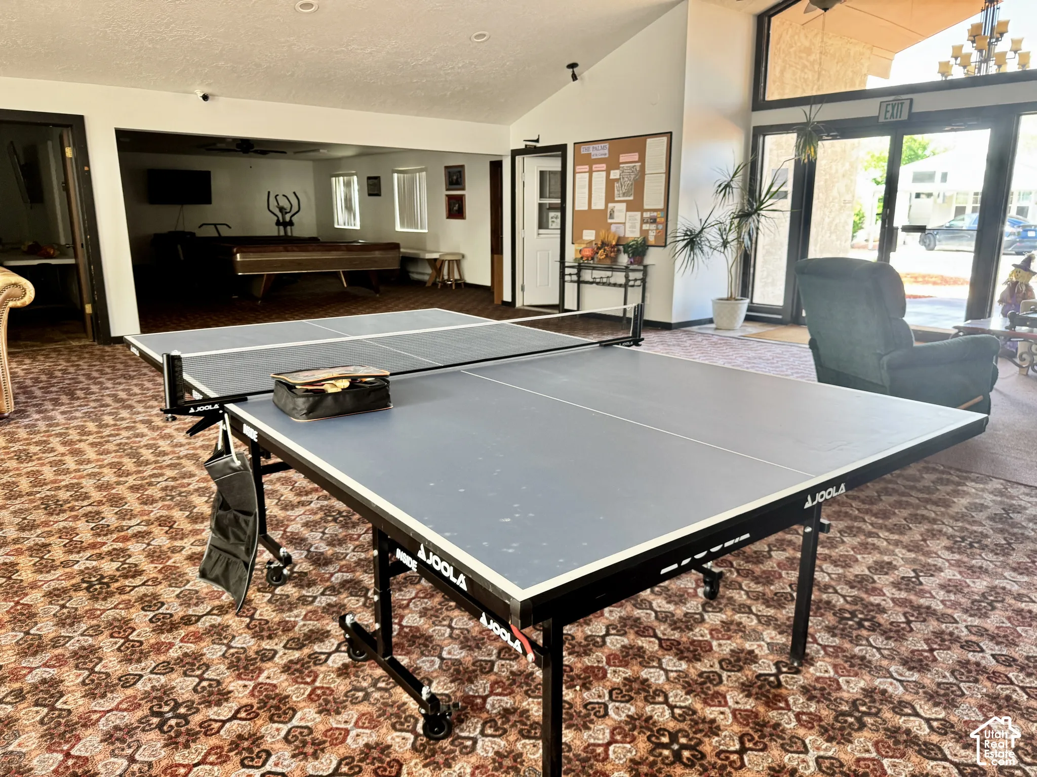 Multi-purpose room featuring vaulted ceilings, patterned wall-to-wall carpeting, and a large multi-pane glass entrance door with a transom window