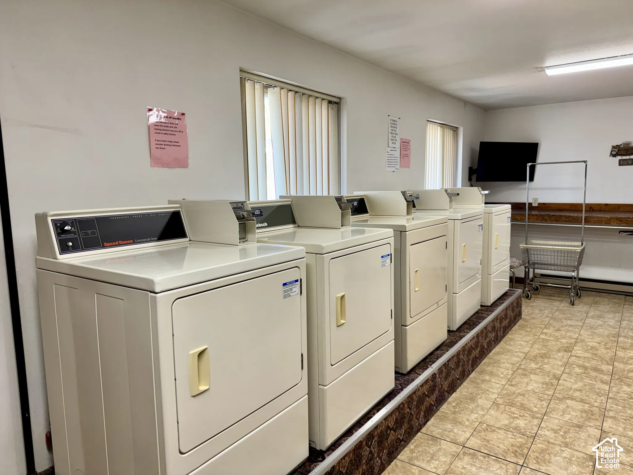 Laundry facility featuring multiple industrial-grade clothes dryers, elevated platform flooring, tile flooring, and a wooden built-in folding counter