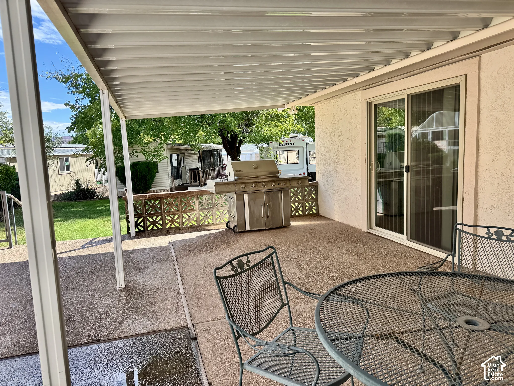 Covered concrete patio featuring a built-in stainless steel grill and a decorative breeze block privacy wall