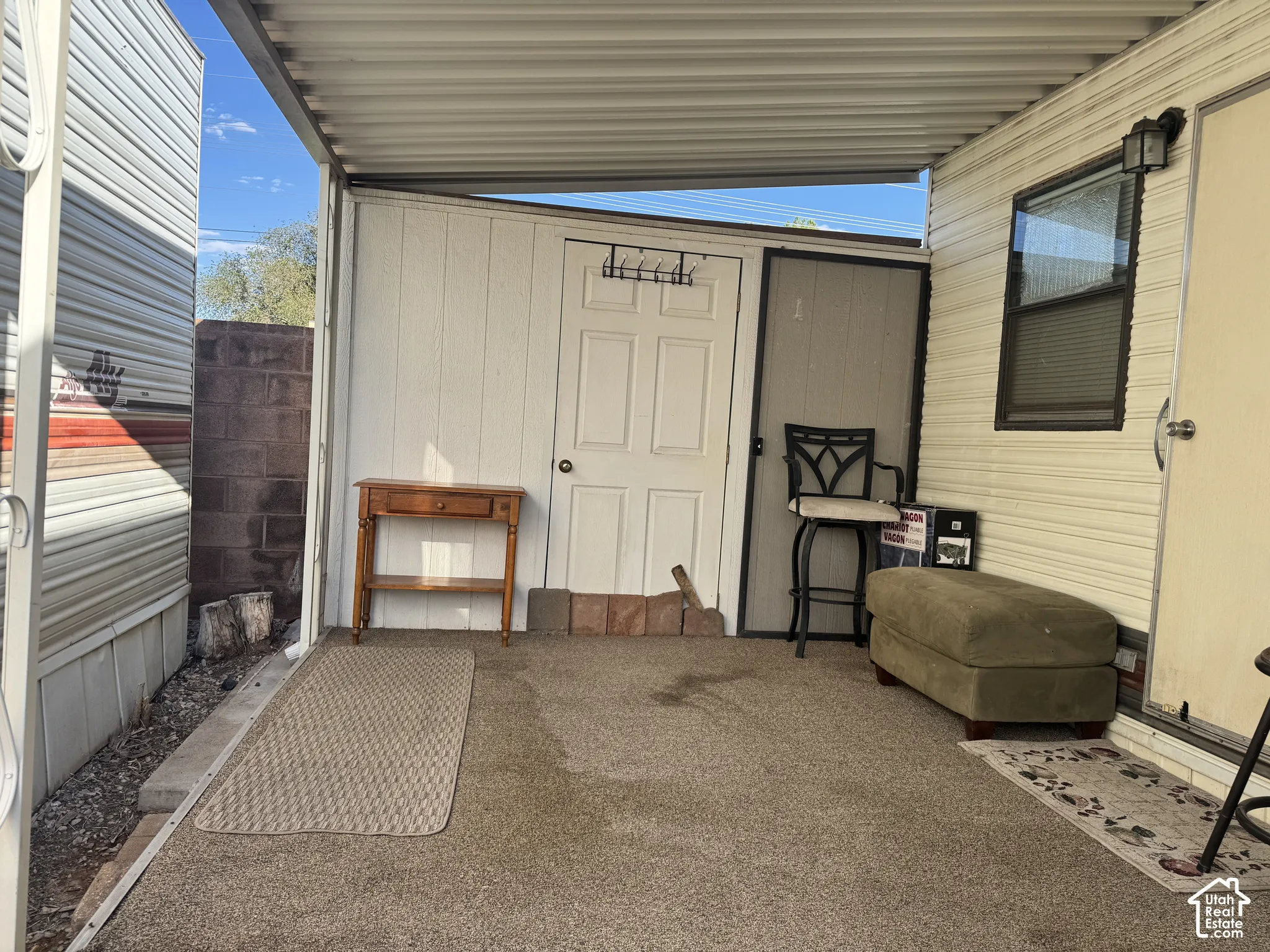 Covered outdoor patio area featuring a textured concrete surface, integrated storage space, and exterior lighting fixture