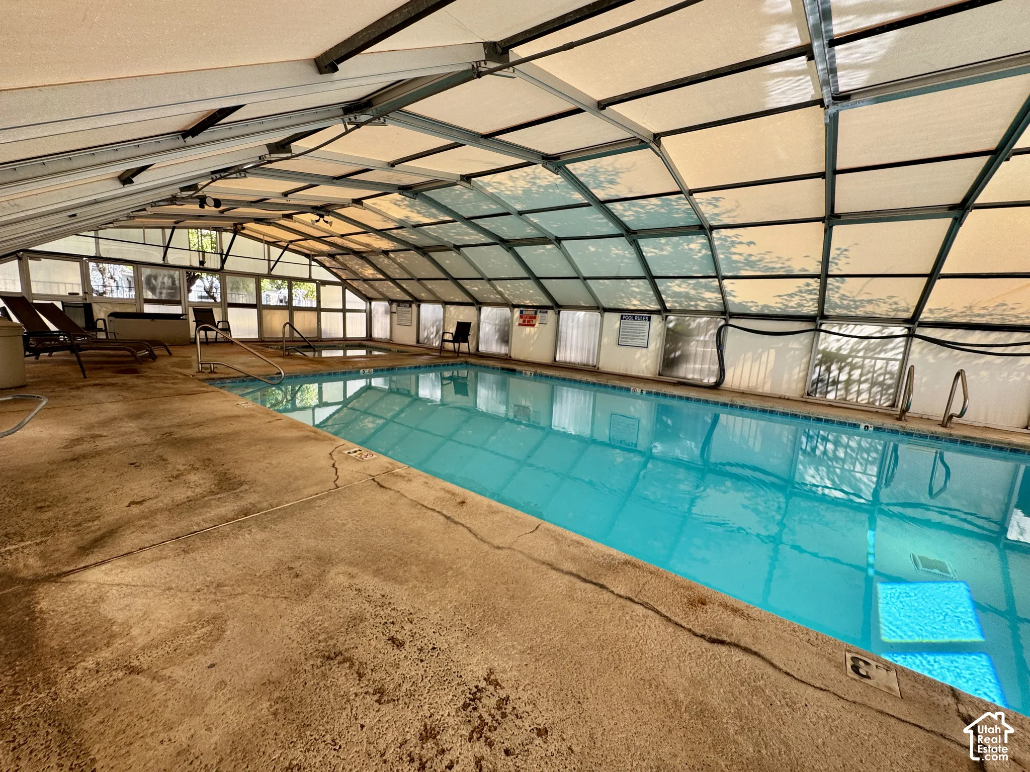 Enclosed swimming pool featuring a retractable arched metal framework, concrete decking, and integrated step entry