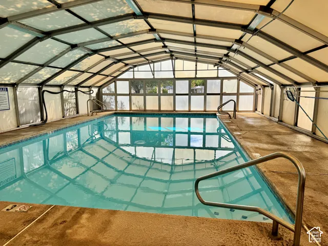 Indoor swimming pool enclosure with a metal-framed roof structure, translucent panels, and perimeter stainless steel handrails