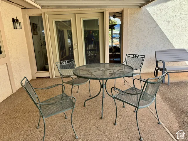 Covered patio featuring concrete flooring, stucco exterior walls, dual-glass panel doors with sidelights, and a wall-mounted light fixture